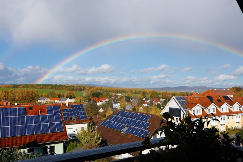 A view over a few houses with solar panels and a rainbow in the sky